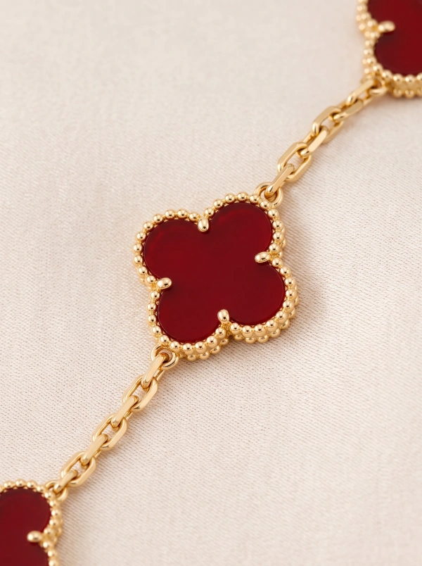 Red clover bracelet detail with a beaded gold-tone border and chain links